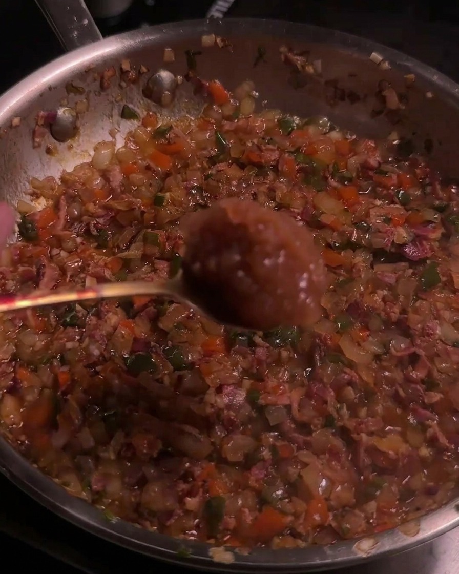 Apfelmus wird von einem Löffel in die karamellisierte Bacon-Chili-Mischung in der Pfanne gegeben.