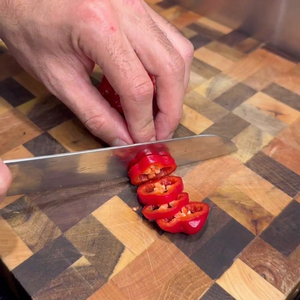 Eine Person schneidet frische rote scharfe Chilis auf einem Holzschneidebrett in Ringe.