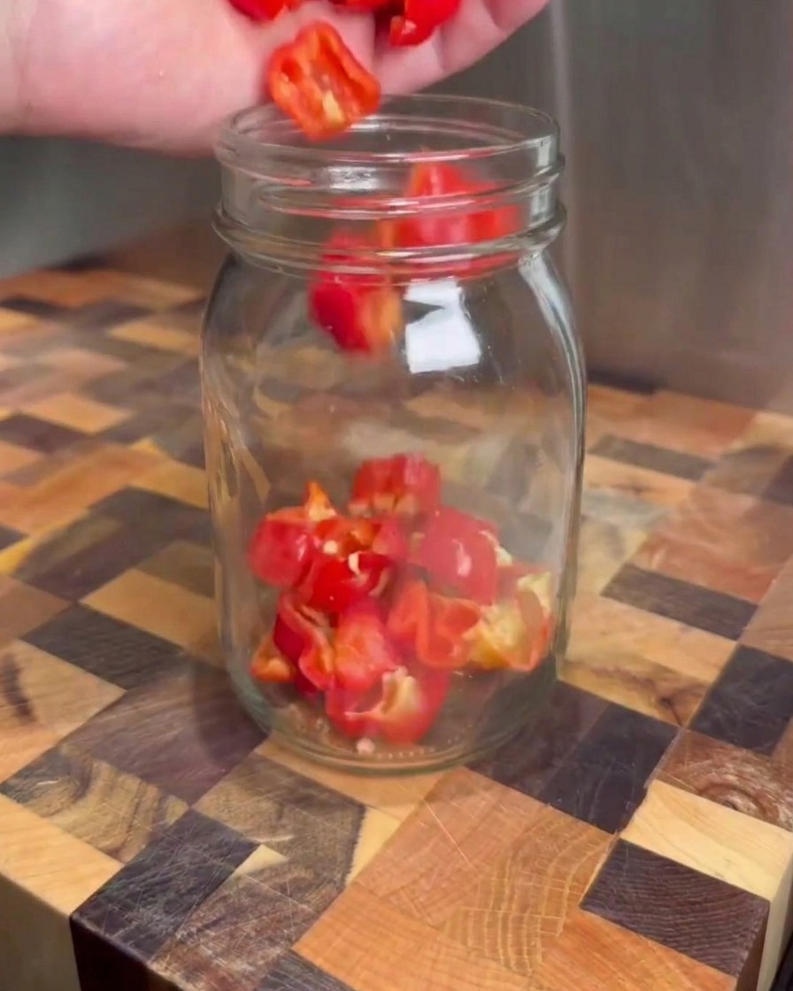 Gehackte rote Chilis werden auf einem Schneidebrett in ein klares Einmachglas gegeben.