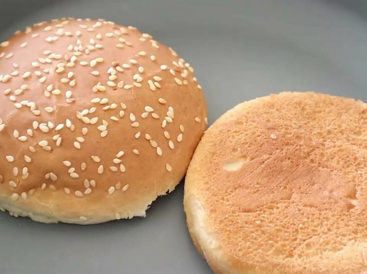 Zwei Hälften eines Sesam-Burgerbrötchens nebeneinander, wovon eine eine schön getoastete, goldbraune Innenseite zeigt.