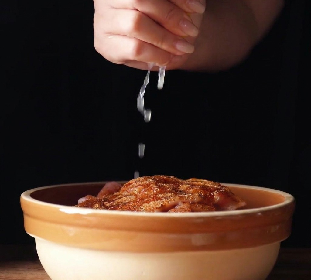Frischer Zitronensaft wird aus einer Zitronenspalte über gewürzte Hähnchenkeulen in einer Keramikschüssel gepresst.