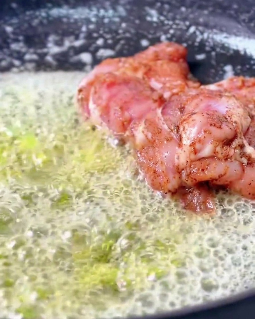 Marinerte Cajun-Hähnchenschenkel braten in einer Pfanne, die mit reichlich brodelnder, schäumender geschmolzener Butter gefüllt ist.