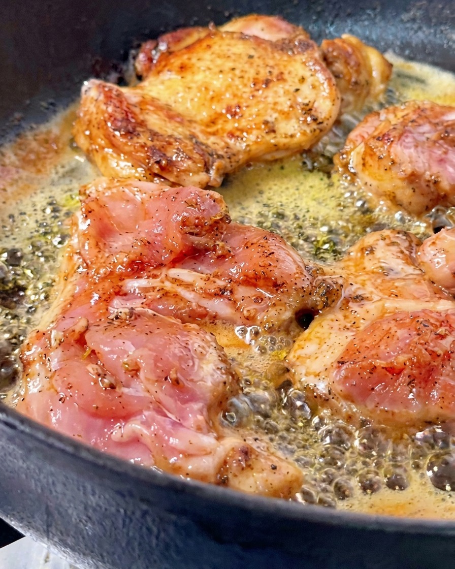 Hähnchenschenkel braten in sprudelnder Butter in einer gusseisernen Pfanne, wobei ein Stück umgedreht wurde und eine knusprige, goldbraune Kruste zeigt.