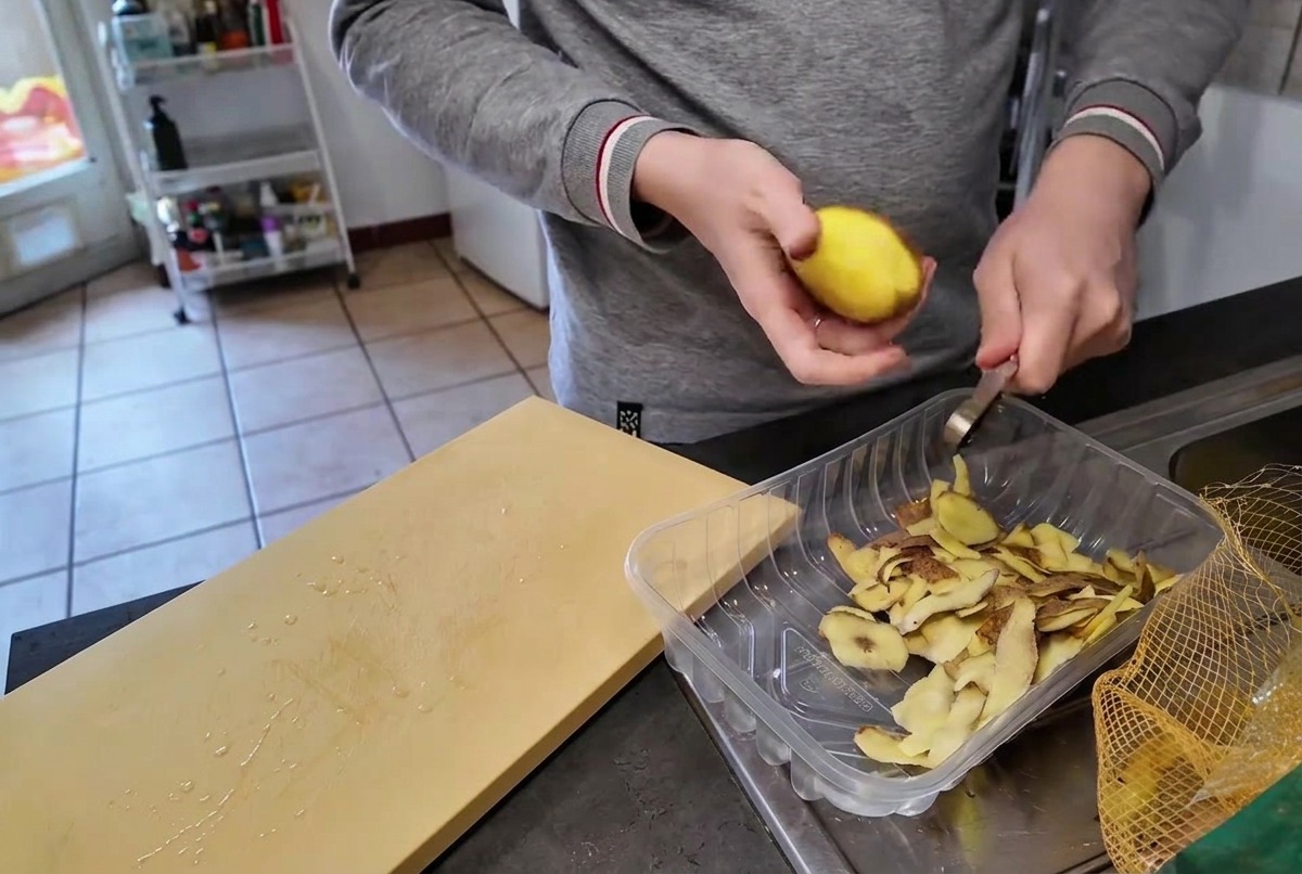 Eine Person schält eine rohe gelbe Kartoffel mit einem kleinen Messer über einem Behälter für die Schalen.