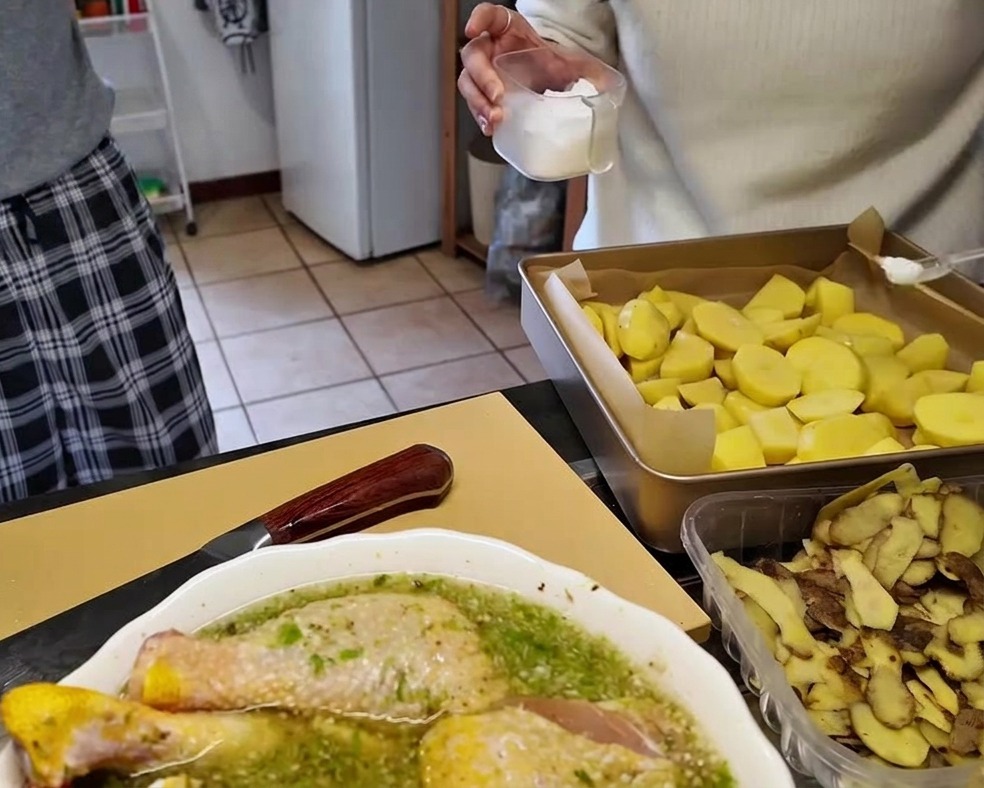 Rohe Kartoffelstücke auf einem mit Backpapier ausgelegten Backblech, die mit Salz aus einem klaren Streuer gewürzt werden.