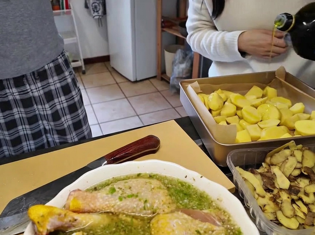 Olivenöl wird aus einer Glasflasche auf ein Backblech mit geschnittenen Kartoffelstücken gegossen.