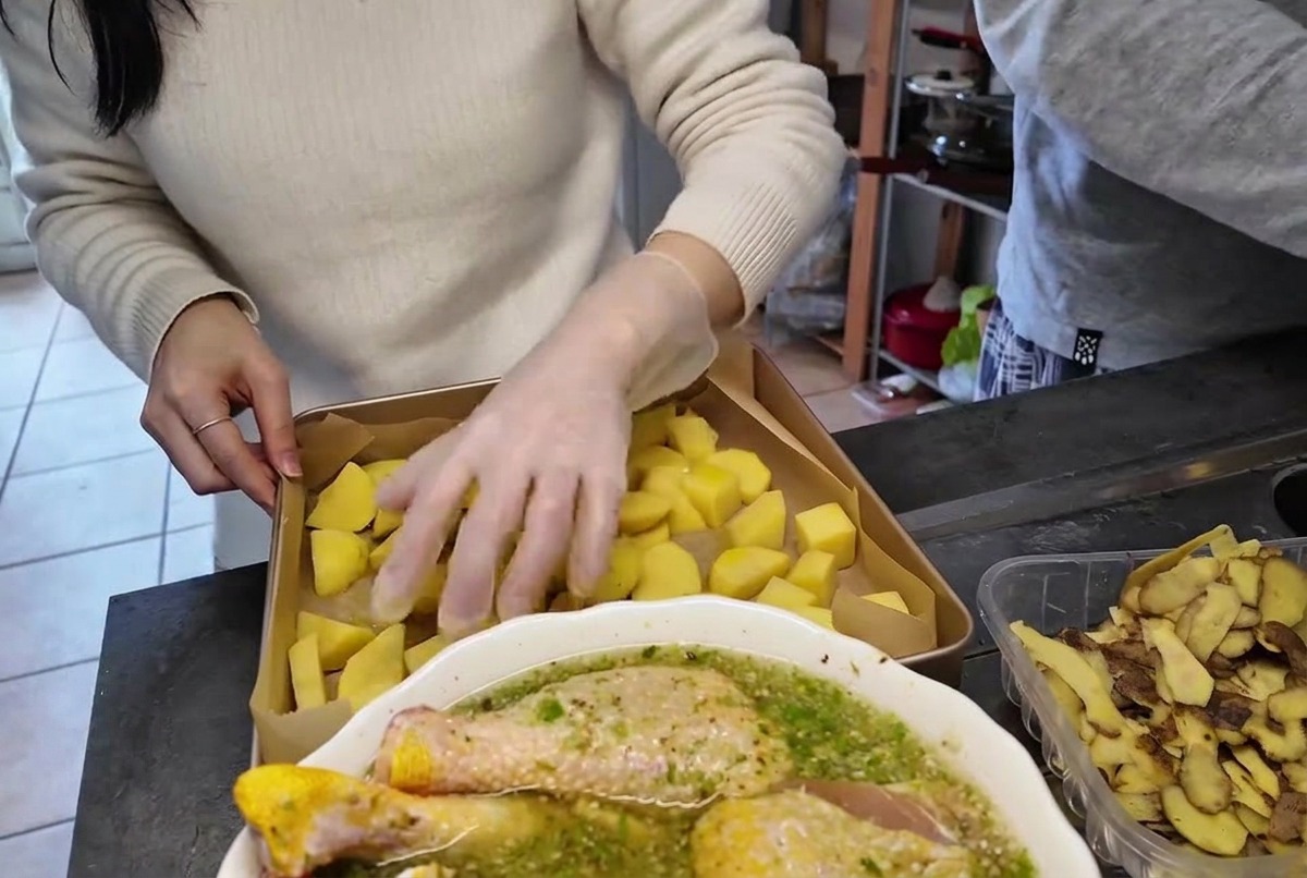 Eine Hand in einem durchsichtigen Plastikhandschuh wendet und vermengt Kartoffelstücke auf einem Backblech.