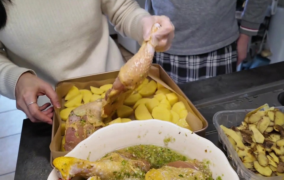 Rohe marinierte Hähnchenschenkel werden mit der Hautseite nach oben auf einer Schicht geschnittener Kartoffeln auf einem Backblech angerichtet.