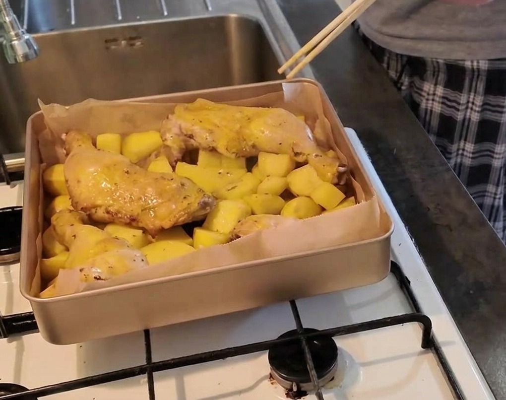 Eine Person sticht mit einem Stäbchen in das Fleisch eines Hähnchenschenkels auf einem Kartoffelbett, um den Garpunkt zu prüfen.