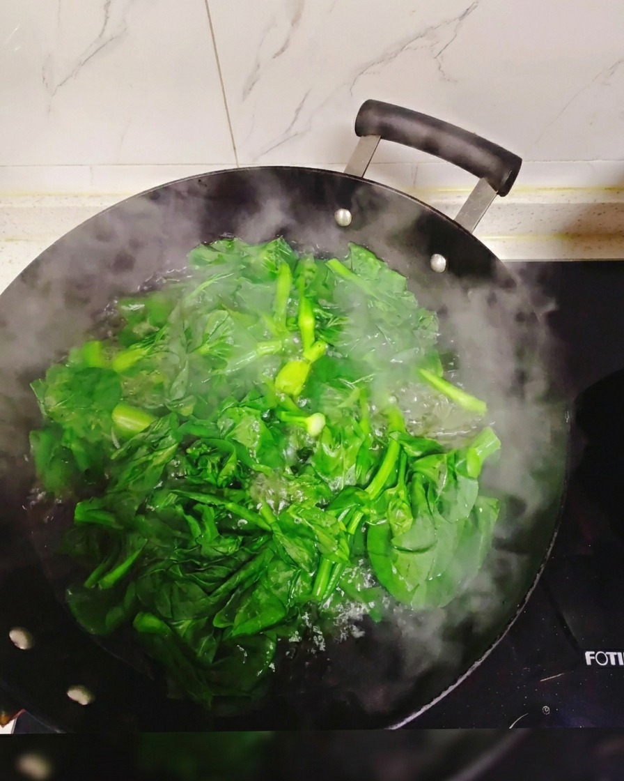 Frisches grünes Blattgemüse, das in einem großen, mit kochendem, dampfendem Wasser gefüllten Wok blanchiert wird.