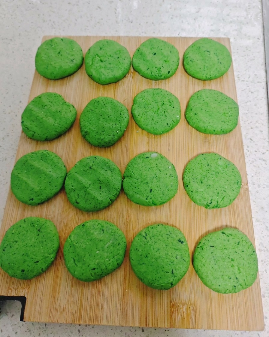 Sechzehn runde, grüne Gemüsetaler, die in einem ordentlichen Gittermuster auf einem Holzschneidebrett angeordnet sind.