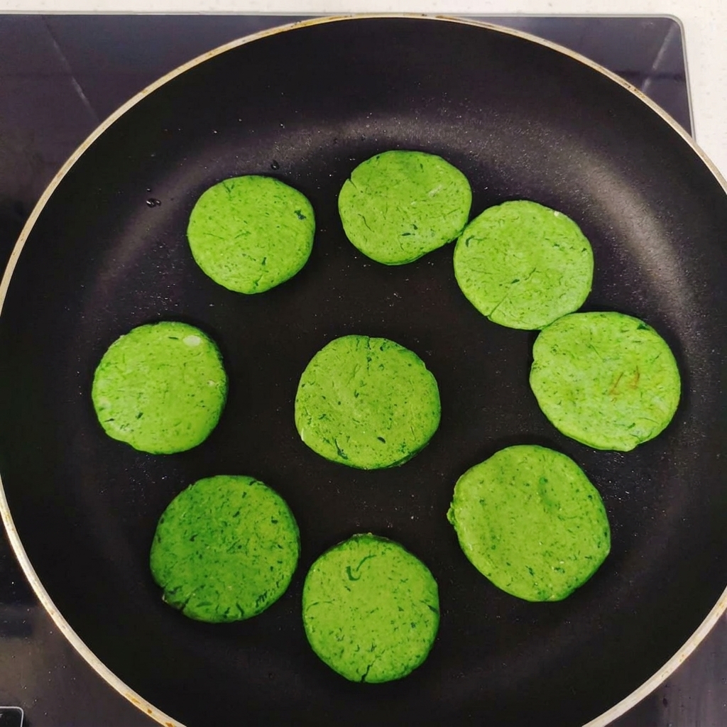 Mehrere runde, grüne Pfannkuchen-Taler, die vor dem Backen im Kreis in einer schwarzen, beschichteten Bratpfanne liegen.