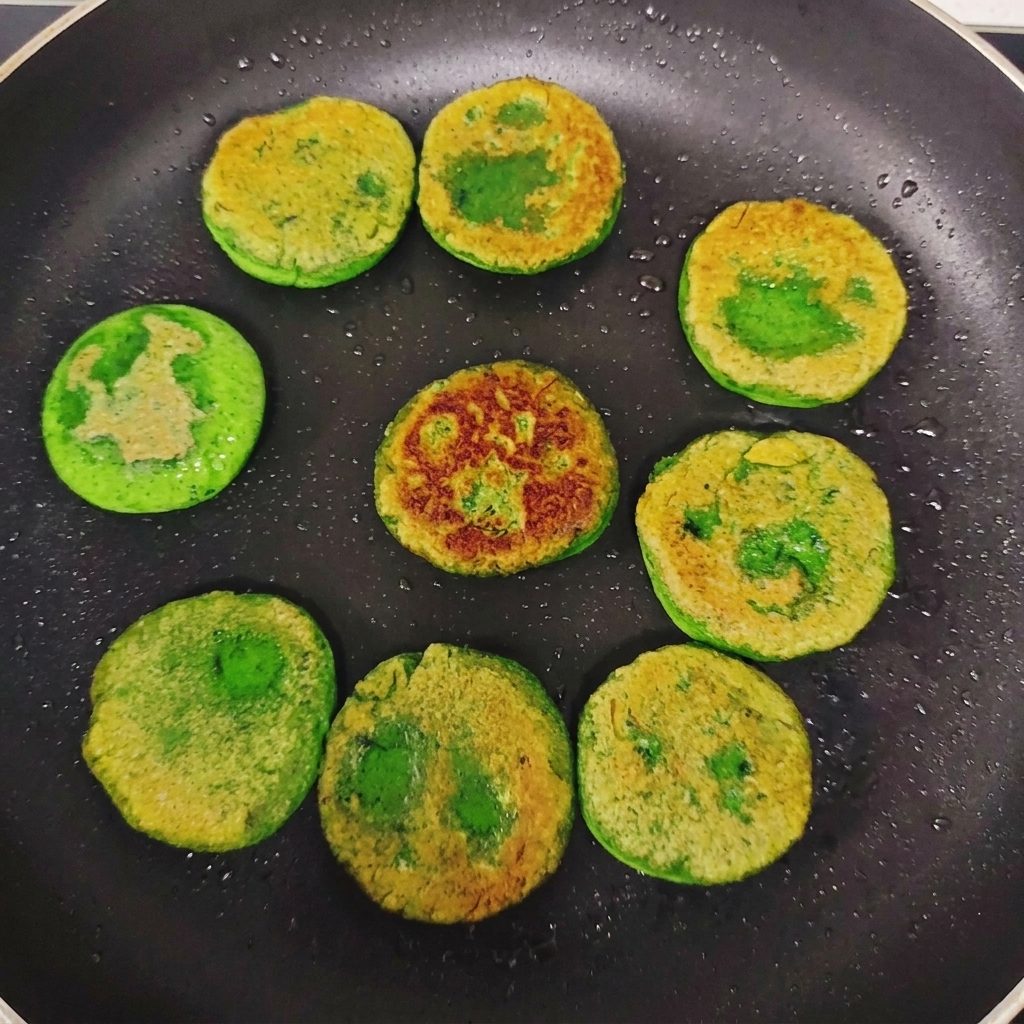 In einer Bratpfanne gewendete grüne Gemüsepfannkuchen, die auf der Oberseite unregelmäßige, goldbraun gebratene Krusten zeigen.