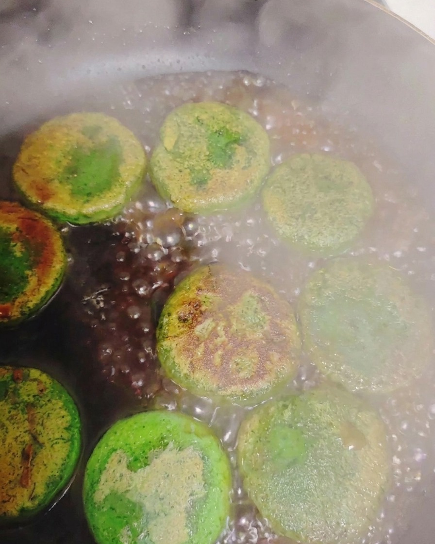 Wasser, das in einer heißen Pfanne um angebratene grüne Gemüsepfannkuchen herum sprudelt und Dampf erzeugt.
