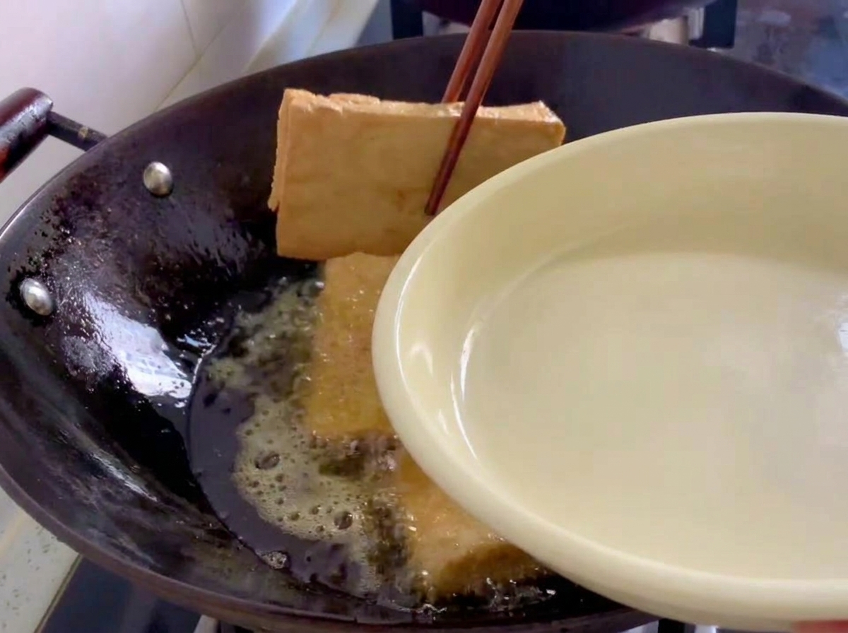 Goldbraun frittierte Tofublöcke werden mit Holzstäbchen aus einem Wok gehoben.