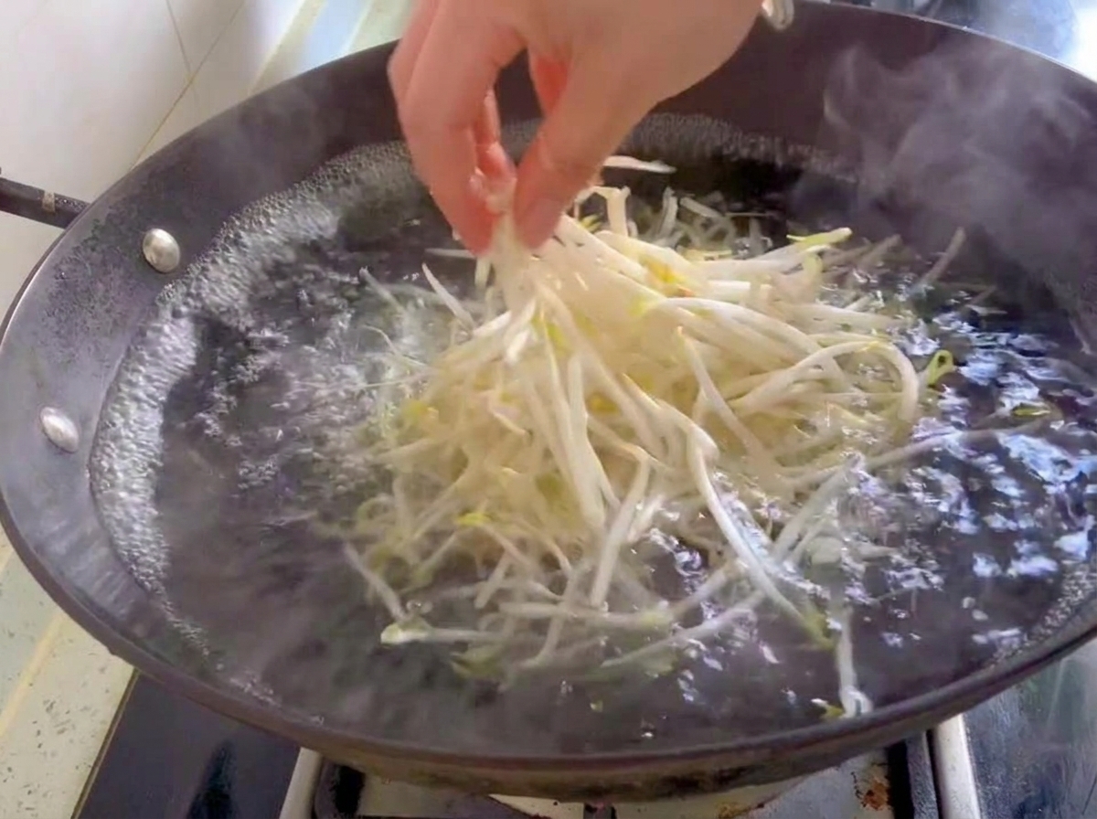 Eine Handvoll frische weiße Mungobohnensprossen wird in einen Wok mit kochendem Wasser gegeben.