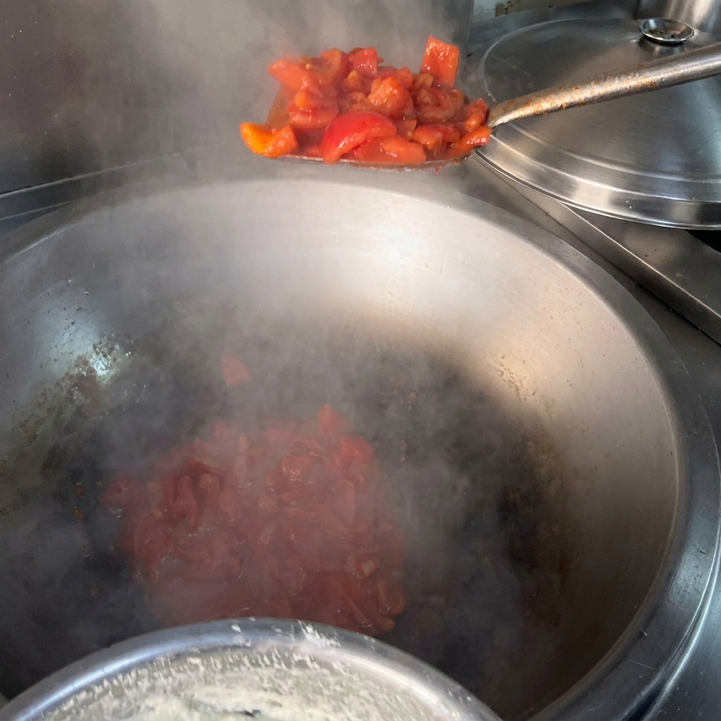 Ein Pfannenwender gibt gewürfelte rote Tomaten in einen großen, dampfenden Wok mit heißem Öl.