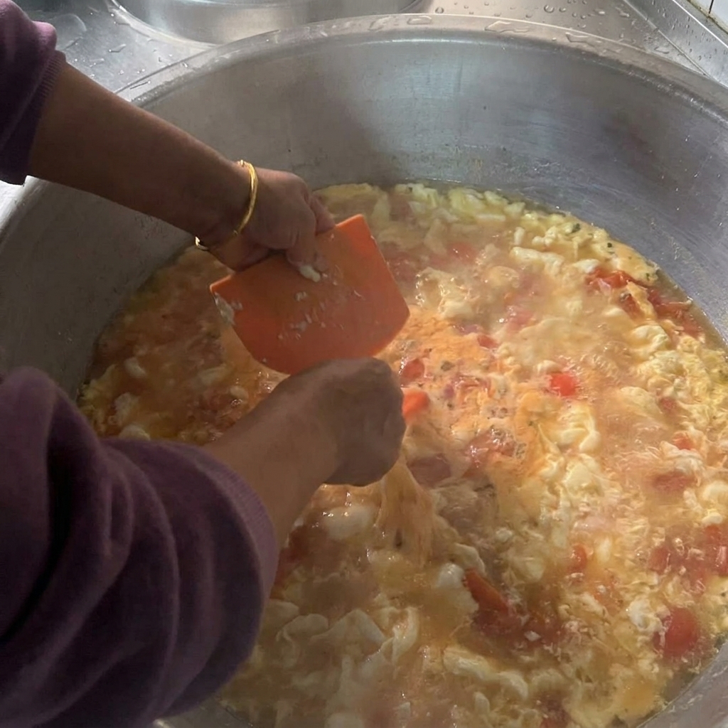 Hände schaben mit einer orangefarbenen Teigkarte kleine Portionen des feuchten Teigs in einen großen Topf mit kochender Suppe.