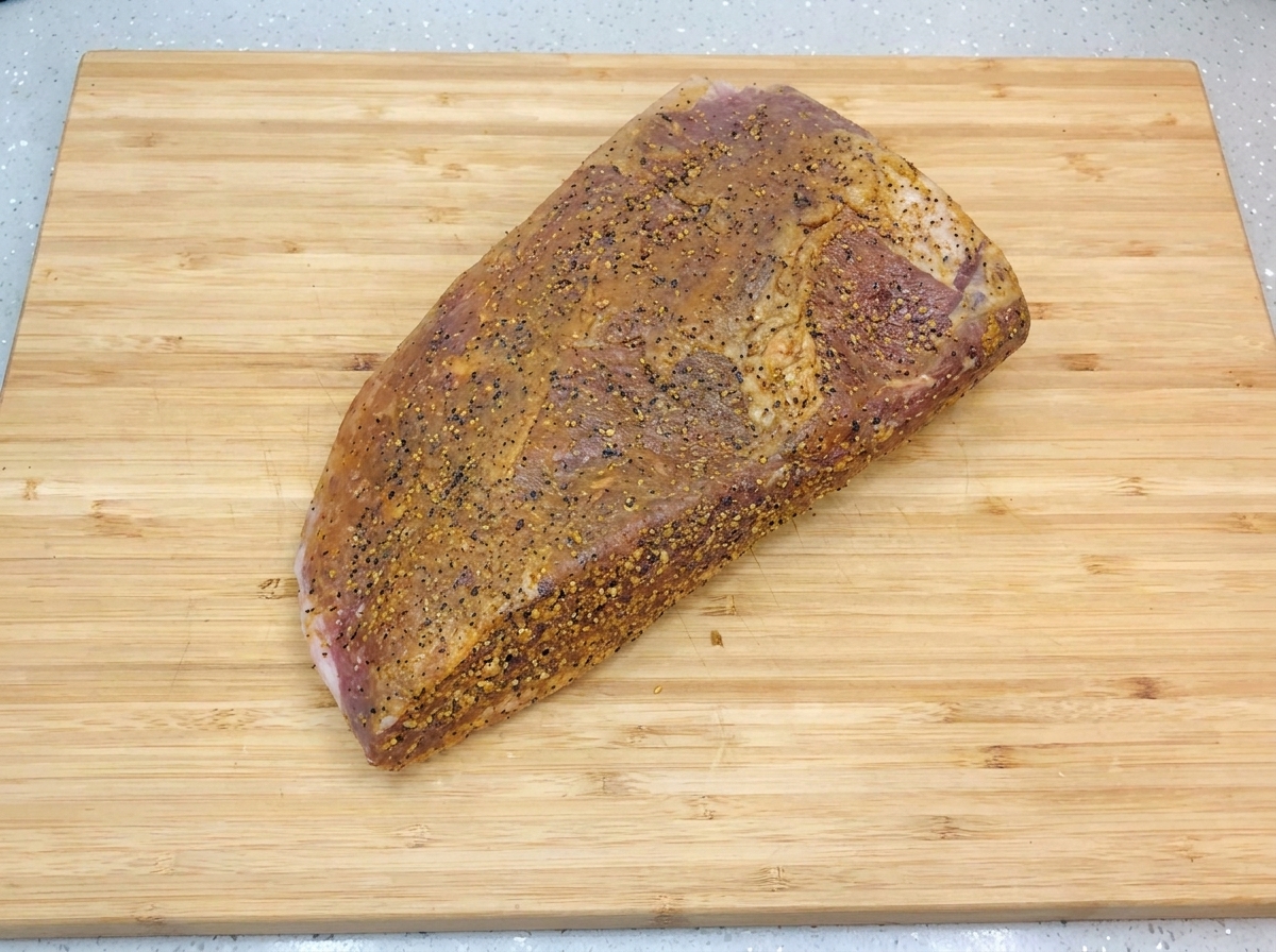Die marinierte Rinderbrust liegt auf einem hellen Holzschneidebrett und glänzt mit einer frischen Schicht Öl und grobem schwarzem Pfeffer.