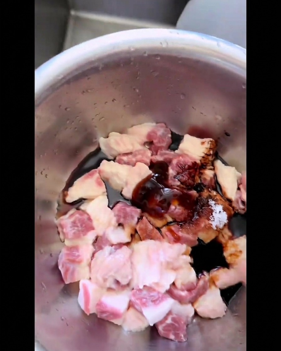 Rohe Stücke von Rinderbrustfett werden in einer Edelstahlschüssel von Hand mit dunkler Marinade, Zucker und Salz vermengt.