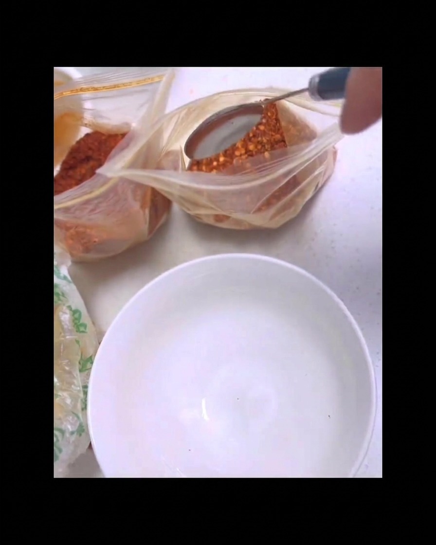 Ein Metalllöffel schöpft rotes Chilipulver aus einer klaren Plastiktüte über einer sauberen weißen Schüssel.