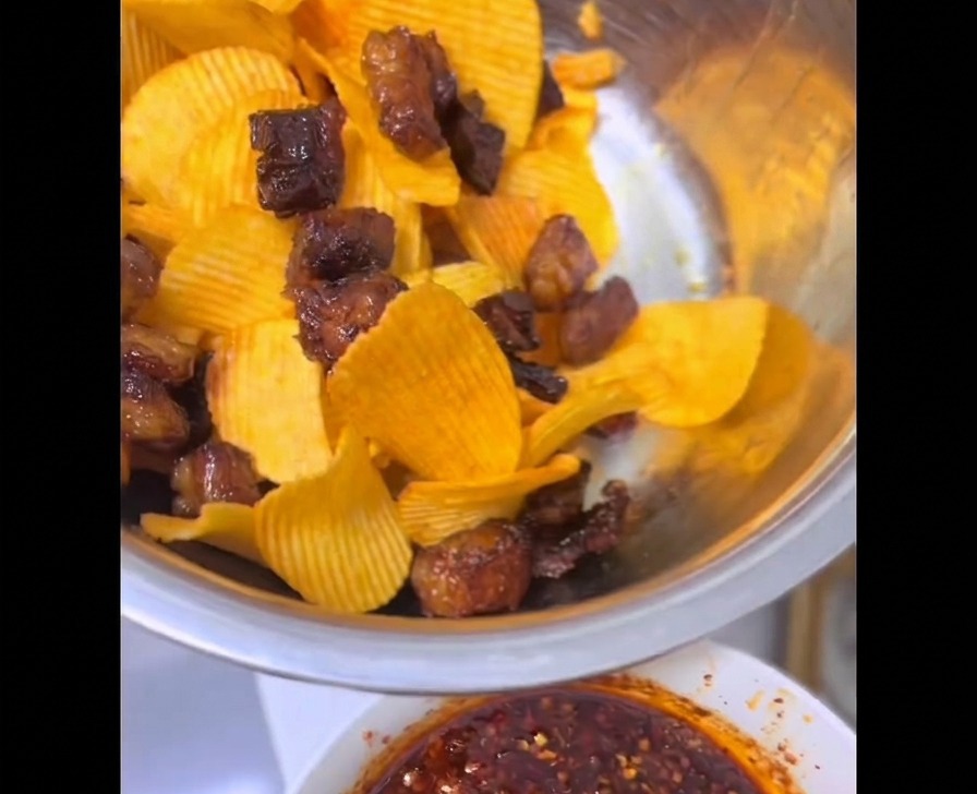 Knusprige Stücke von Rinderbrustfett aus der Heißluftfritteuse vermischt mit hellgelben Riffel-Kartoffelchips in einer Edelstahlschüssel.