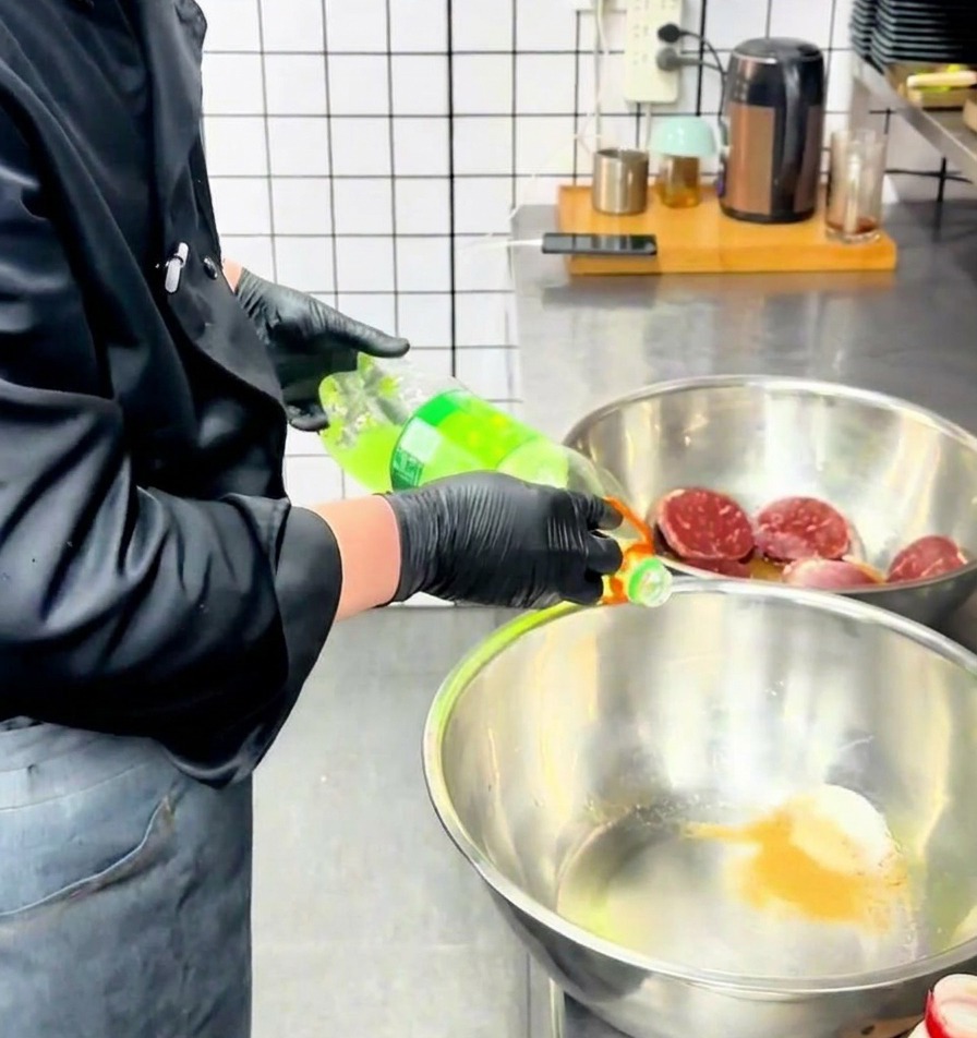 Ein Koch gießt eine klare Flüssigkeit aus einer Flasche in eine Edelstahlschüssel mit Gewürzpulver.