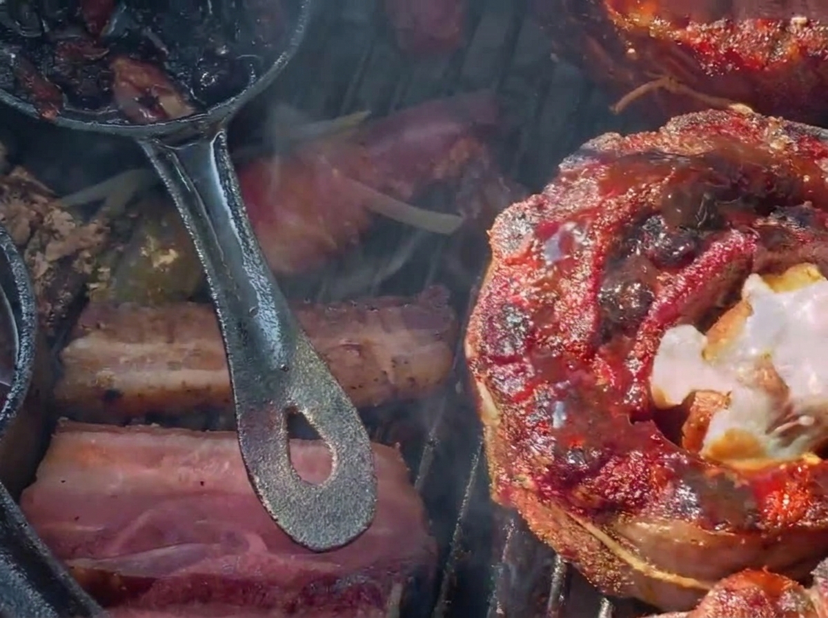 Geriebener Käse schmilzt über einem dunklen, mit Blaubeersauce glasierten, gefüllten Rippchen-Becher auf einem Holzkohlegrill.