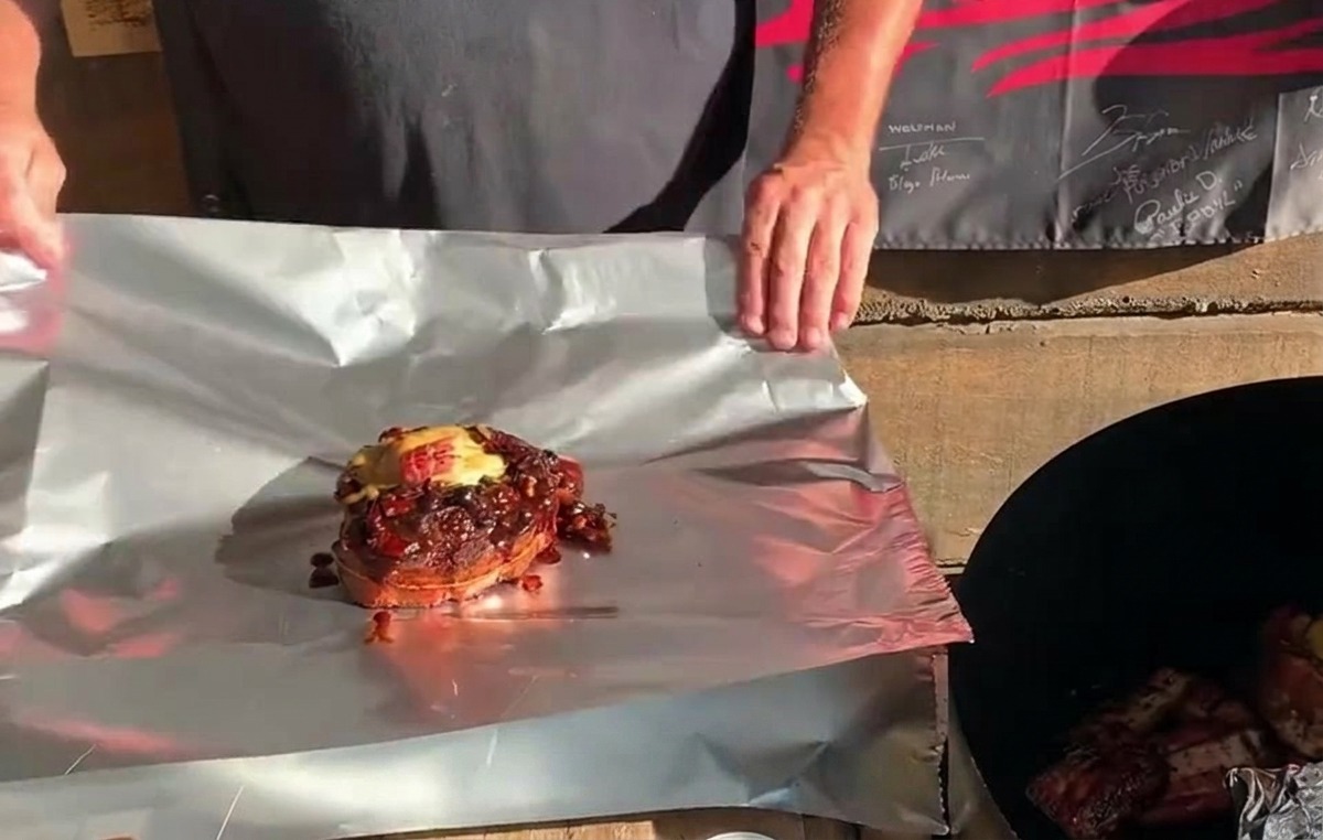 Ein fertig gefüllter St. Louis Rippchen-Becher, garniert mit Käse und Sauce, steht auf einer Alufolie bereit zum Einwickeln.