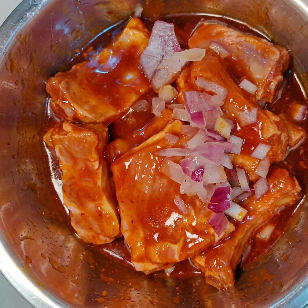 Fein gehackte rote Zwiebeln werden über die marinierten, rohen Schweinerippchen in einer Metallschüssel gestreut.