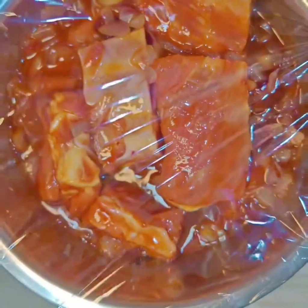 Eine Metallschüssel mit gewürzten Schweinerippchen, fest mit Klarsichtfolie versiegelt.