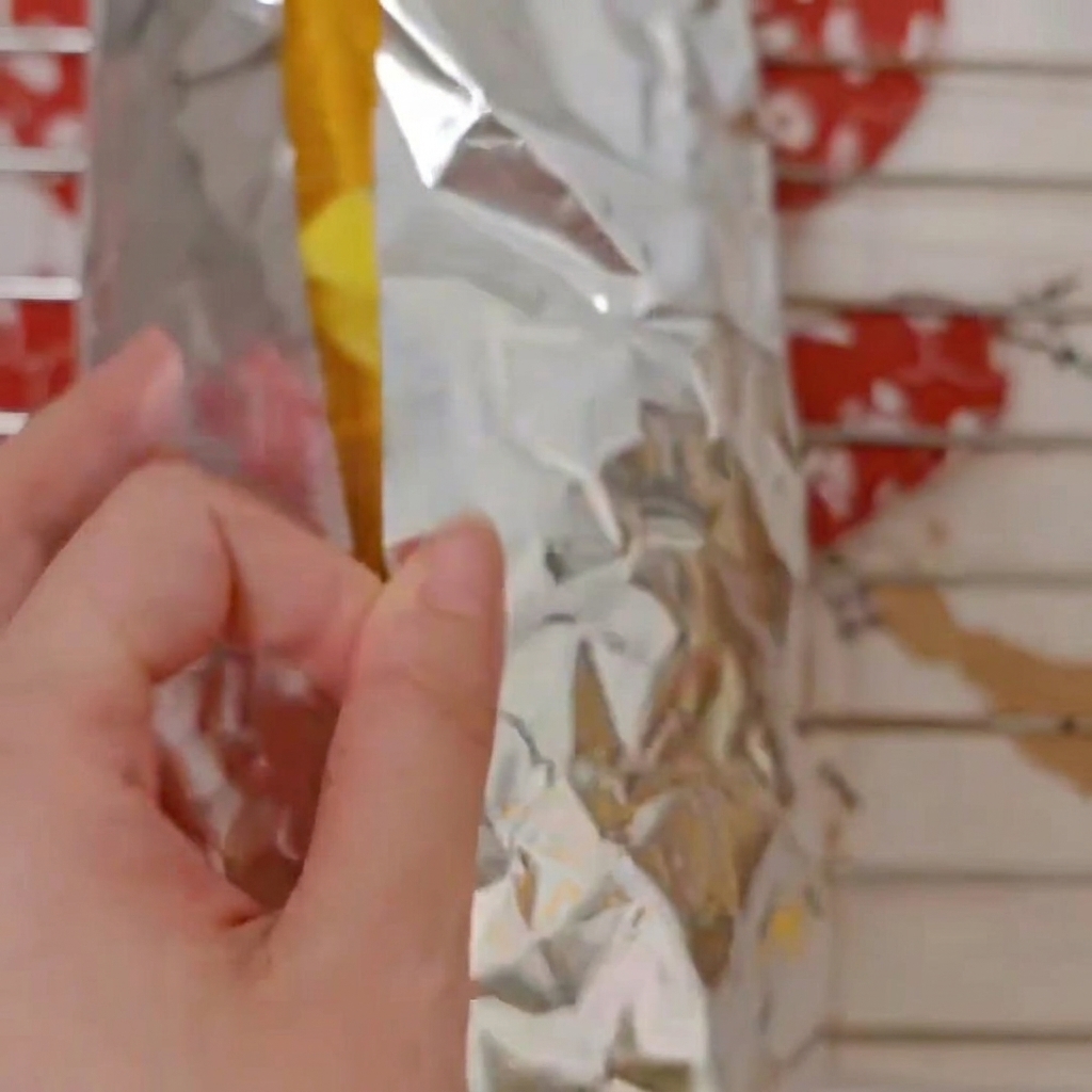Finger falten und wickeln die Zuckermaiskolben in ein Stück silberne Alufolie ein.