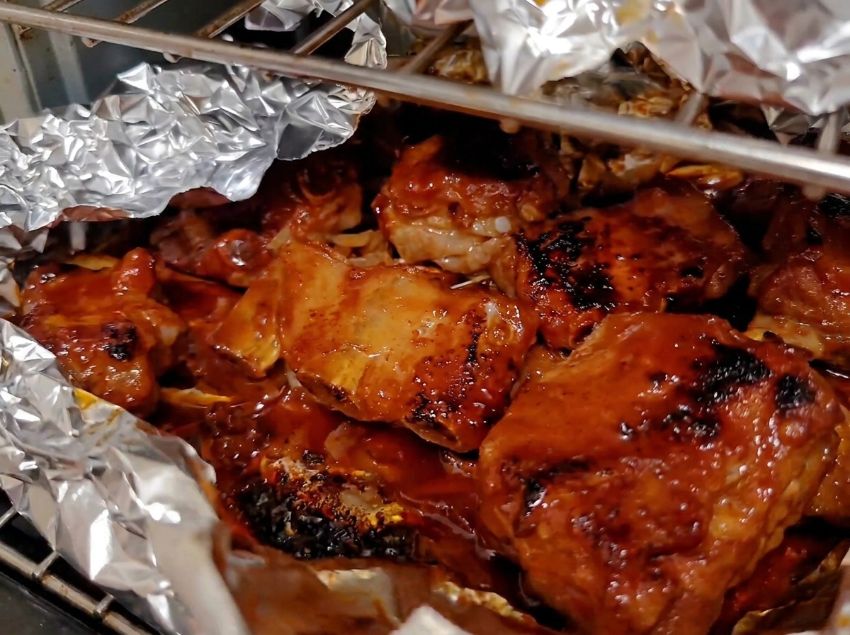 Tief karamellisierte und glasierte Schweinerippchen brodeln in einer geöffneten Alufolie im Ofen.