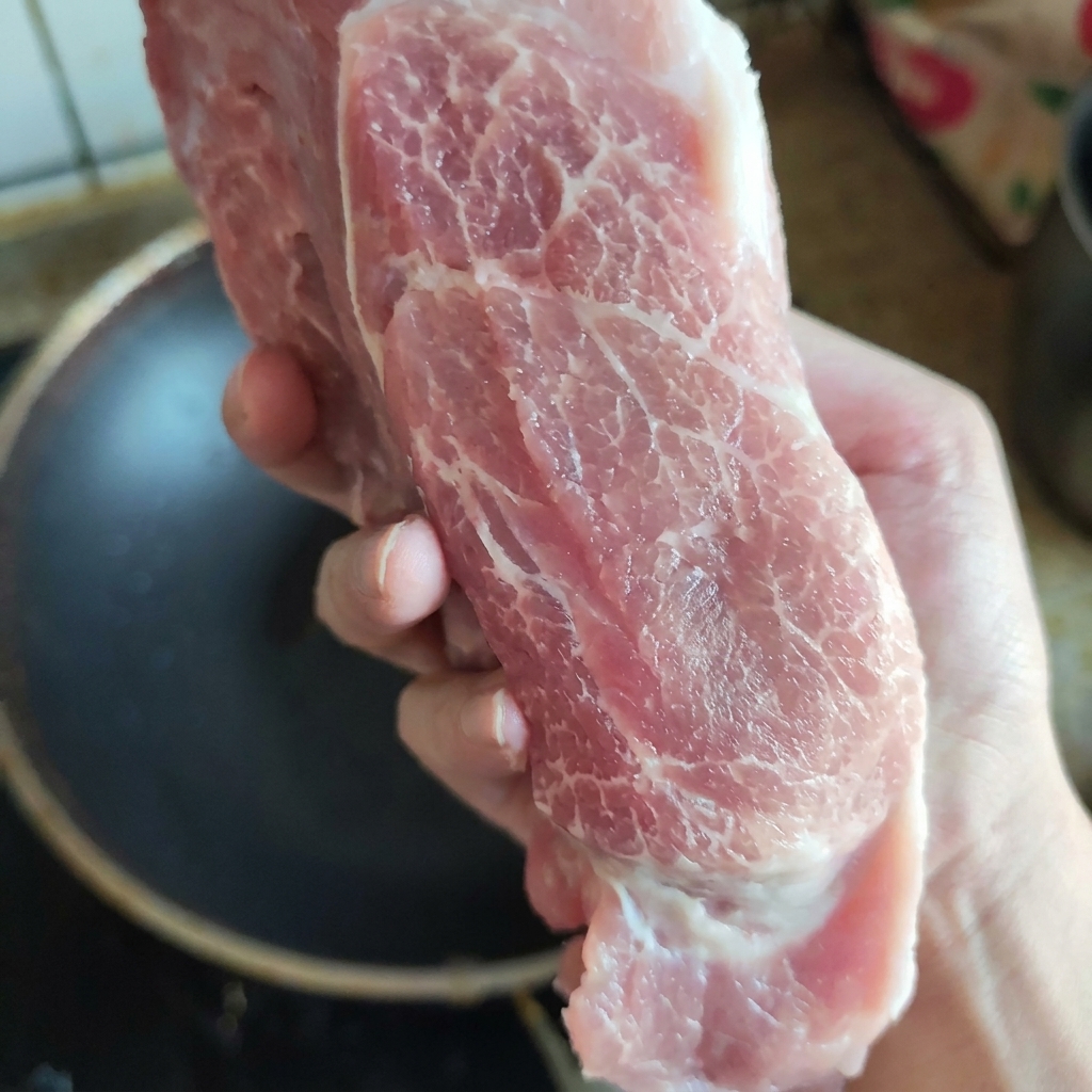 Ein rohes, gut marmoriertes Stück Schweinenacken wird von Hand präsentiert, um die frische Textur und Fettverteilung zu zeigen.