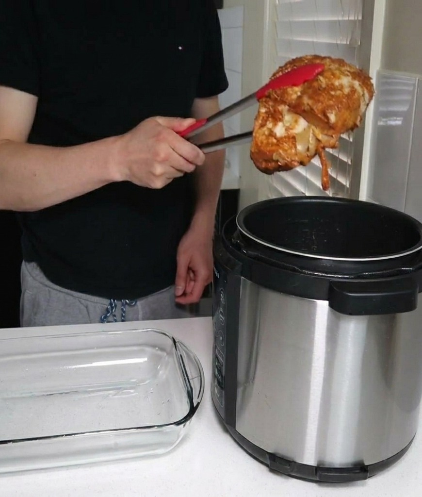 Eine Person hebt mit einer Grillzange ein großes Stück gegarte Schweineschulter aus einem elektrischen Schnellkochtopf neben einer leeren Glasschale.
