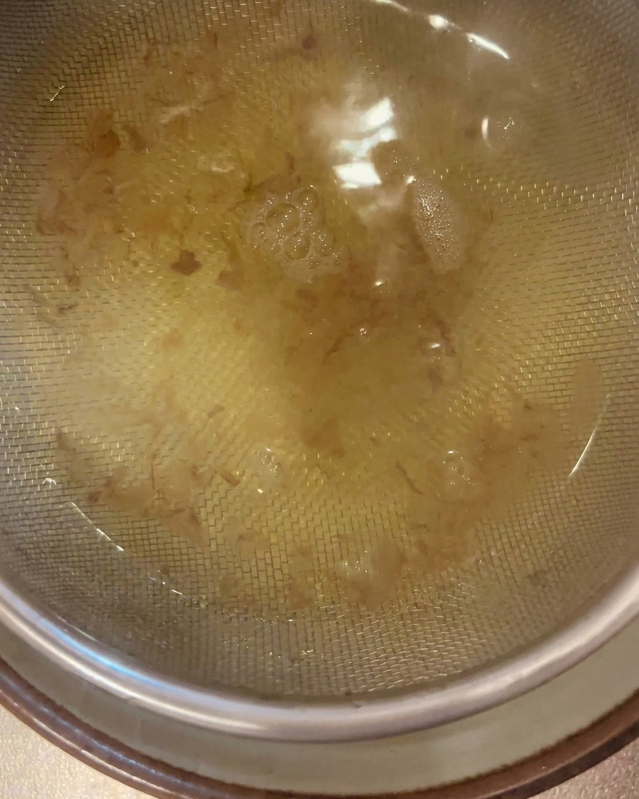 Klare, goldene Dashi-Brühe wird durch ein feines Edelstahlsieb in eine darunter stehende Schüssel gegossen.