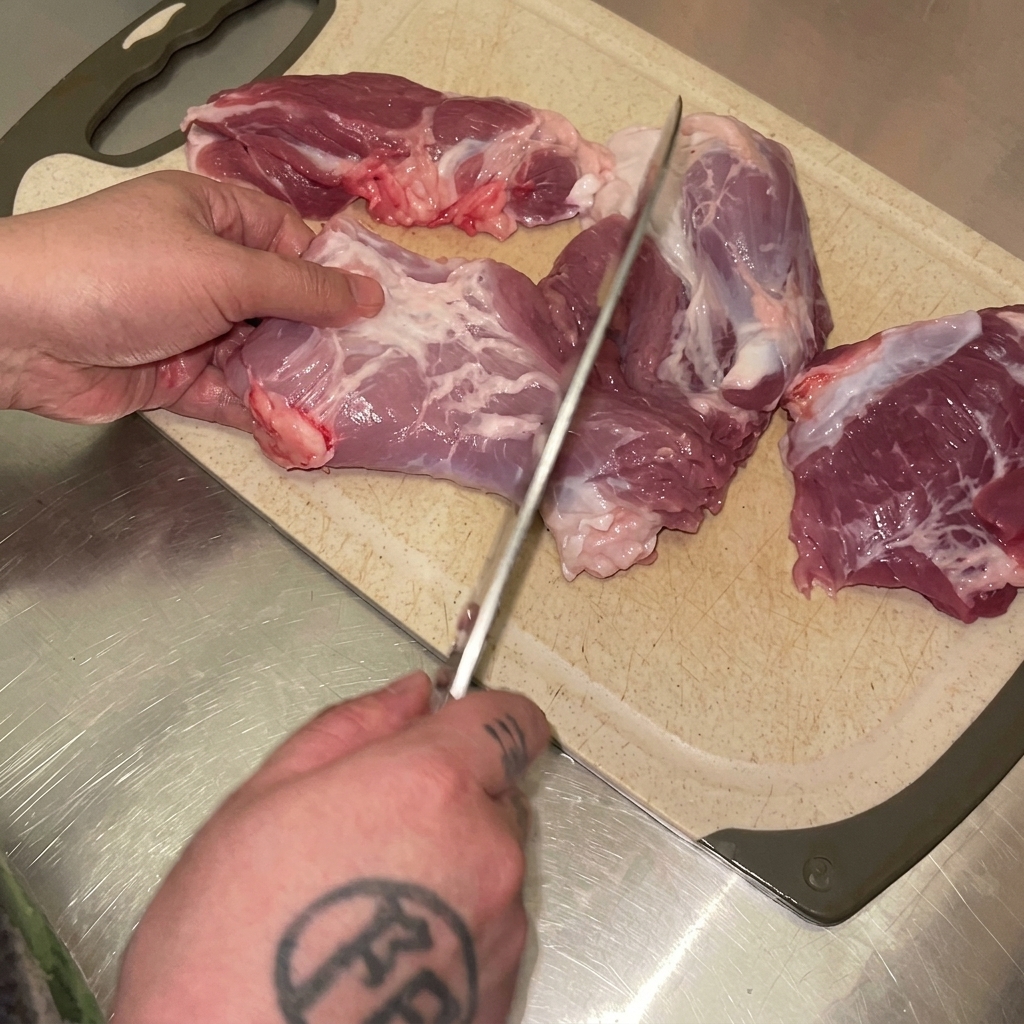 Hände schneiden mit einem Messer rohes Schweinefleisch auf einem Schneidebrett in kleine Stücke.