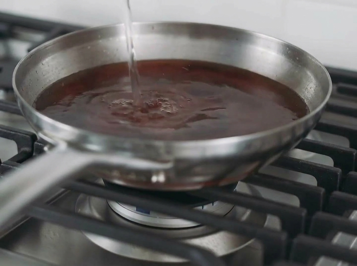 Flüssigkeit wird in eine Pfanne mit gebratenem Hähnchen gegossen, um eine Brühe zu bilden.