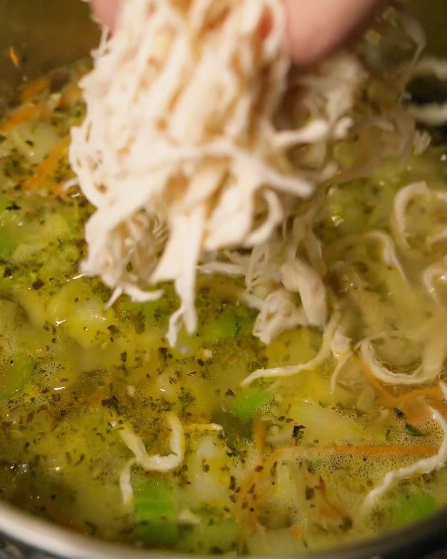 Zerkleinertes Hähnchen wird in die köchelnde Suppe gegeben.