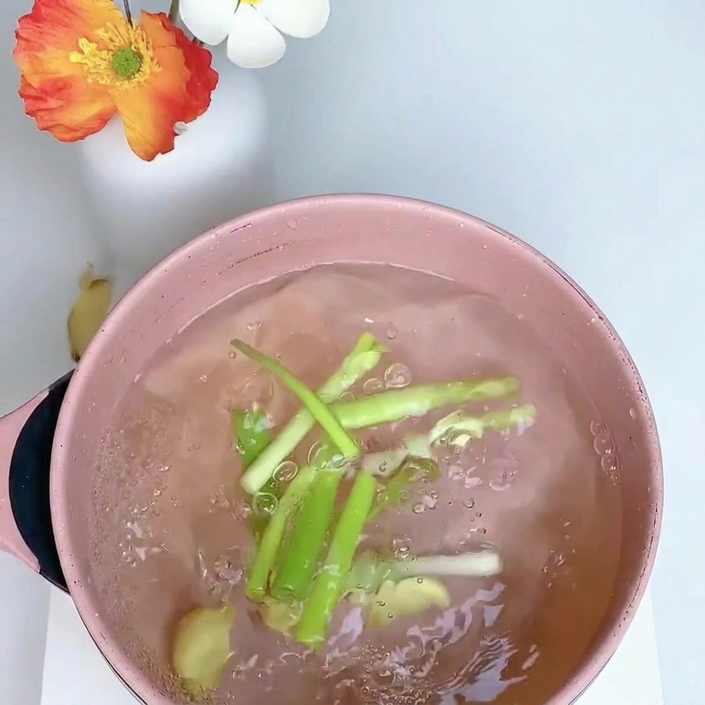 Eine Hähnchenkeule köchelt in einem Topf mit Wasser, Frühlingszwiebeln, Ingwer und Sternanis.