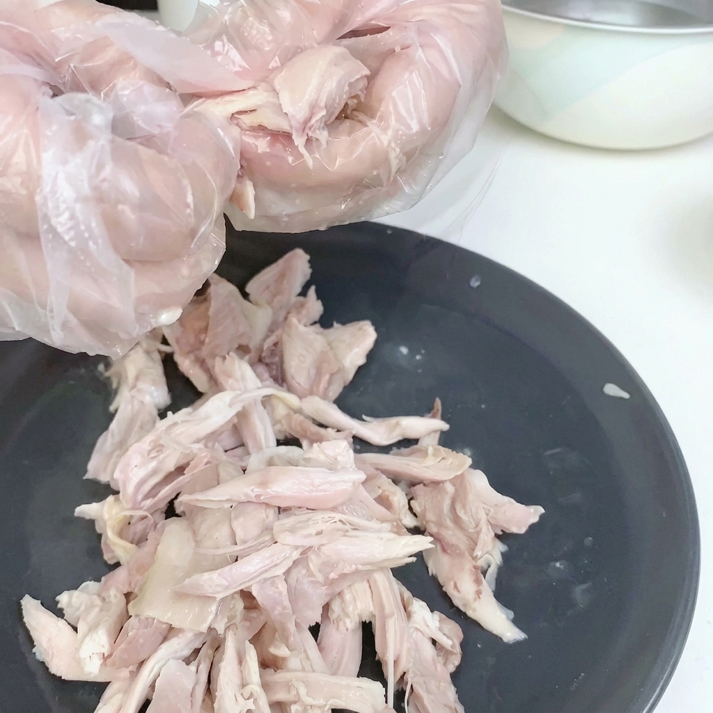 Zerkleinertes Hähnchenfleisch ohne Haut auf einem weißen Teller.
