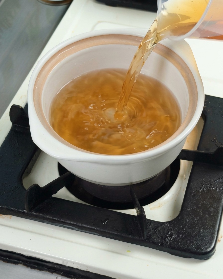 Kombu-Dashi-Brühe wird in einen weißen Keramiktopf gegossen.