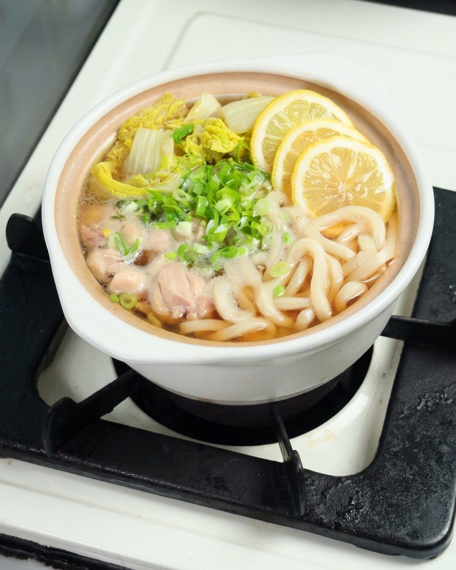 Dünne Zitronenscheiben liegen auf der dampfenden Udon-Suppe.