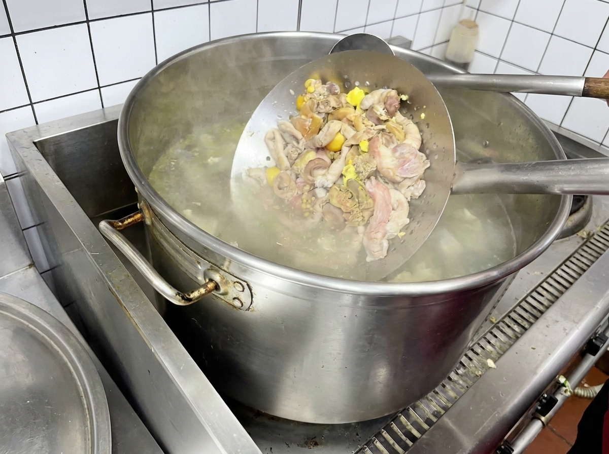 Hühnerinnereien werden in einem Metallsieb über kochendem Wasser blanchiert.