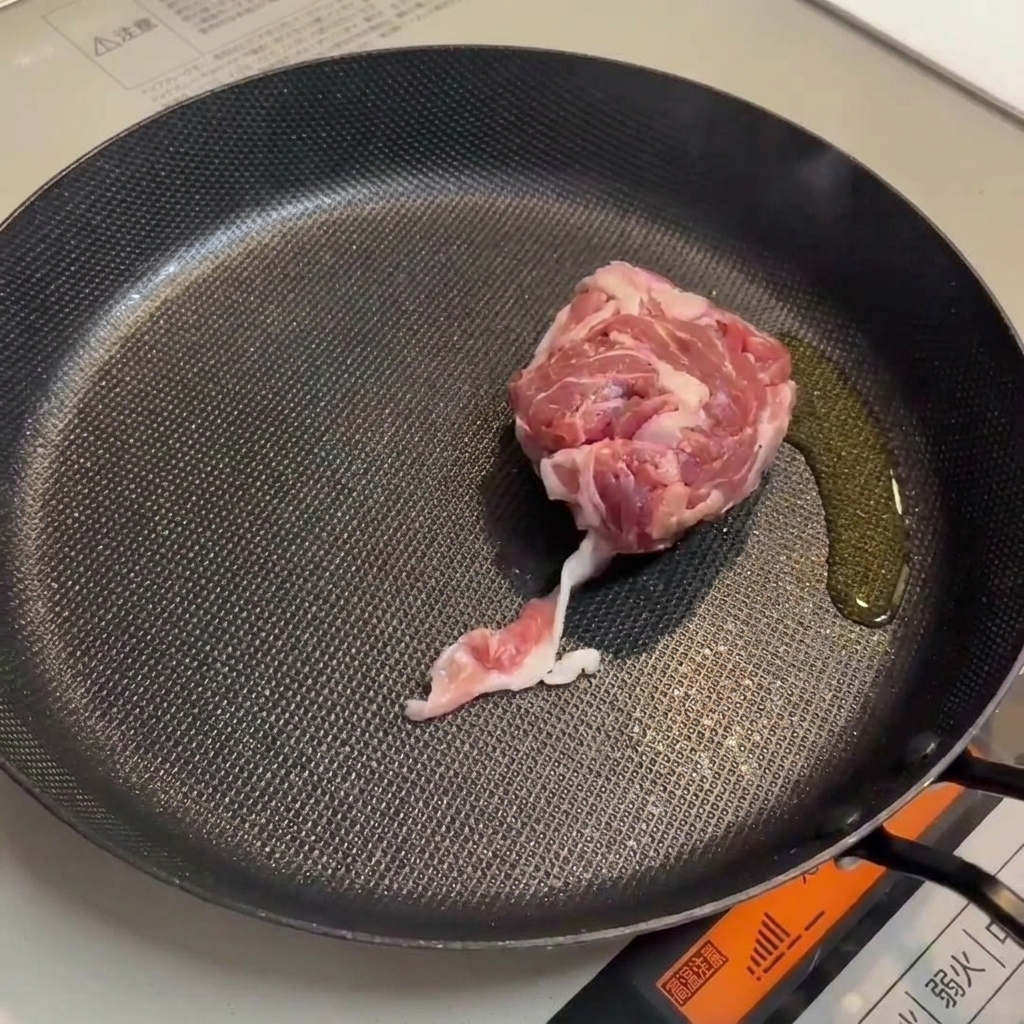 Schweinefleisch und Würstchen bräunen in einer Pfanne.