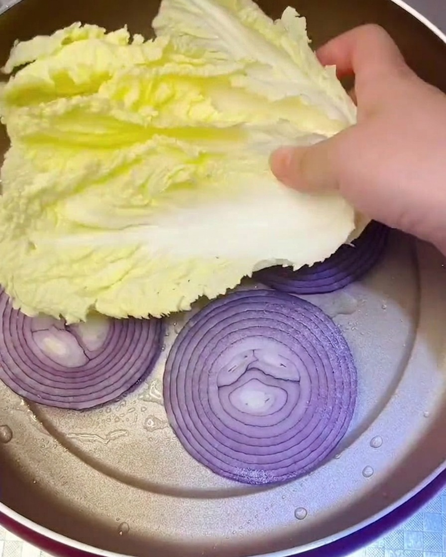 Frische Napakohlblätter werden über die Zwiebeln in die Pfanne gelegt.