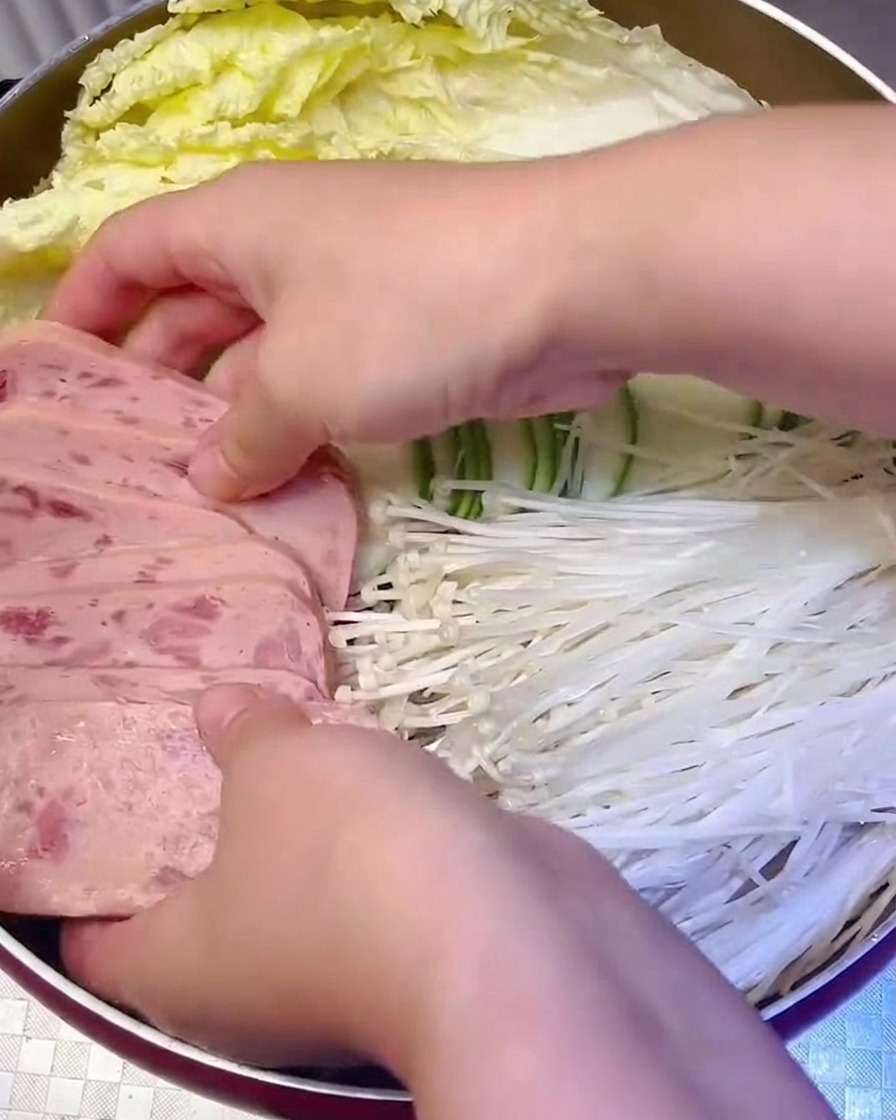 Scheiben von Frühstücksfleisch und Enoki-Pilze werden ordentlich im Topf platziert.