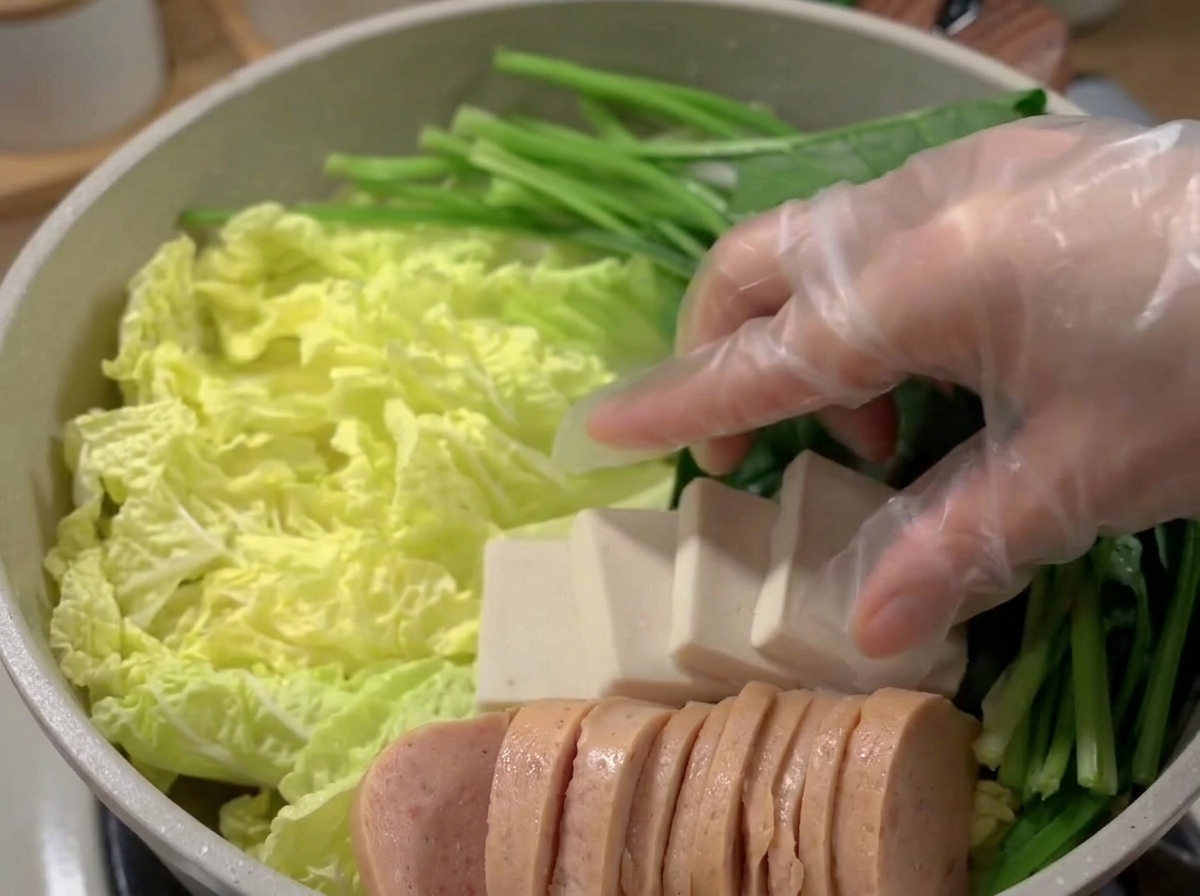 Ein breiter Topf, gefüllt mit einer schönen Anordnung aus Frühstücksfleisch, Tofu, Fischkuchen und Gemüse.
