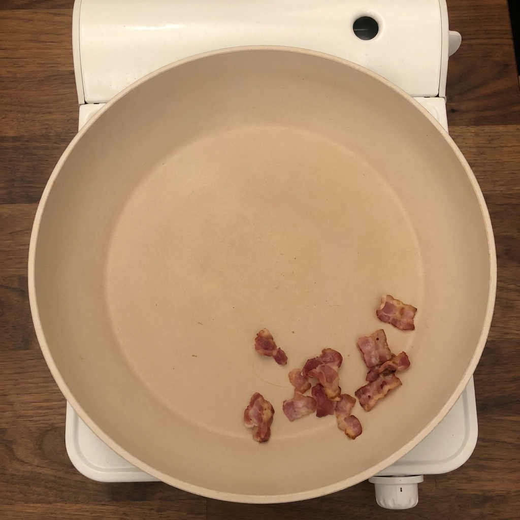 Frisch gehackte Zwiebeln und Sellerie werden zu den knusprigen Speckstücken in die Pfanne gegeben.