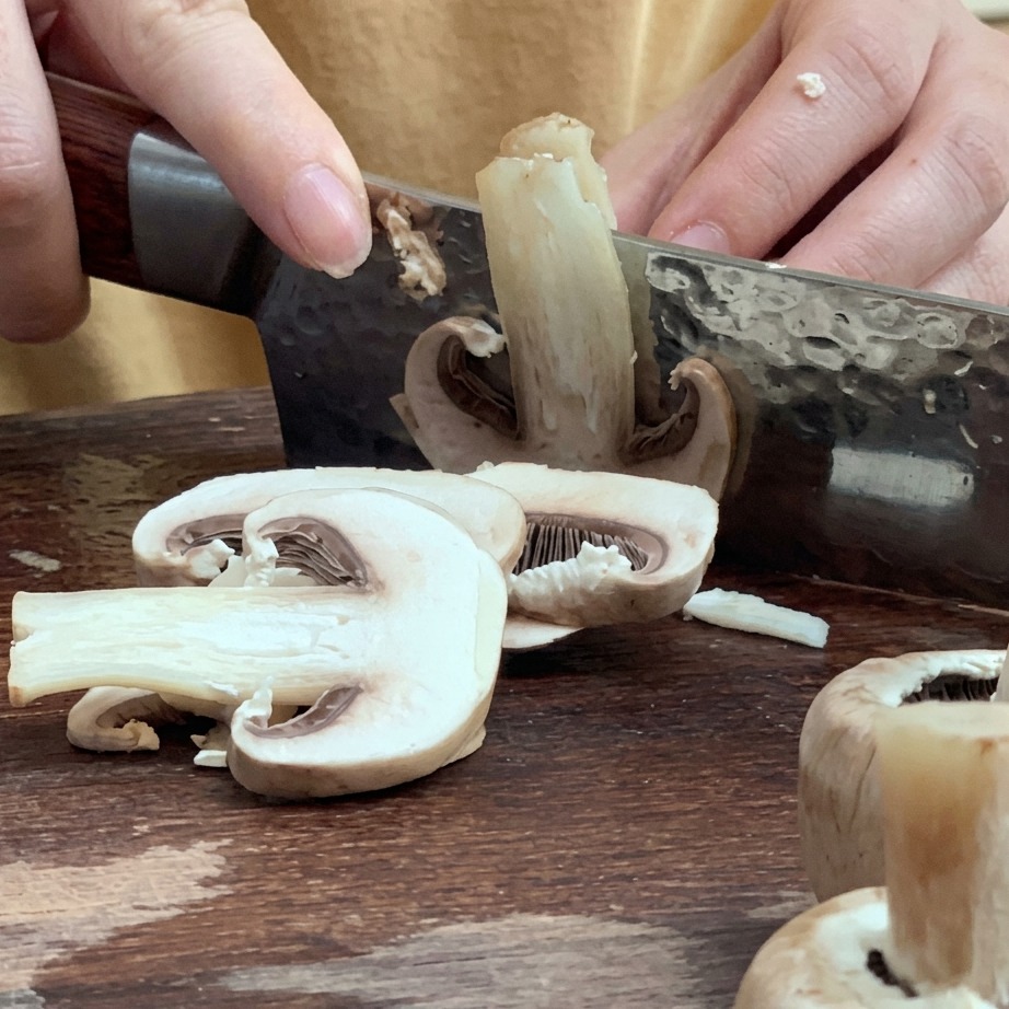 Frische Pilze werden auf einem Holzbrett in dünne Scheiben geschnitten.